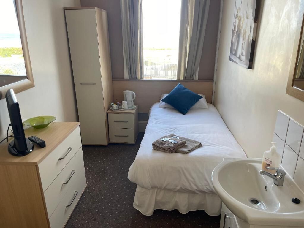 Ett hotellrum med en säng, ett sängbord med en kaffebryggare, en garderob, ett handfat och ett fönster med gardiner.