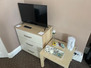 Ett hotellrum med en tv på ett träskåp, ett litet bord med en kaffebryggare, muggar och ett bricka med diverse tillbehör.