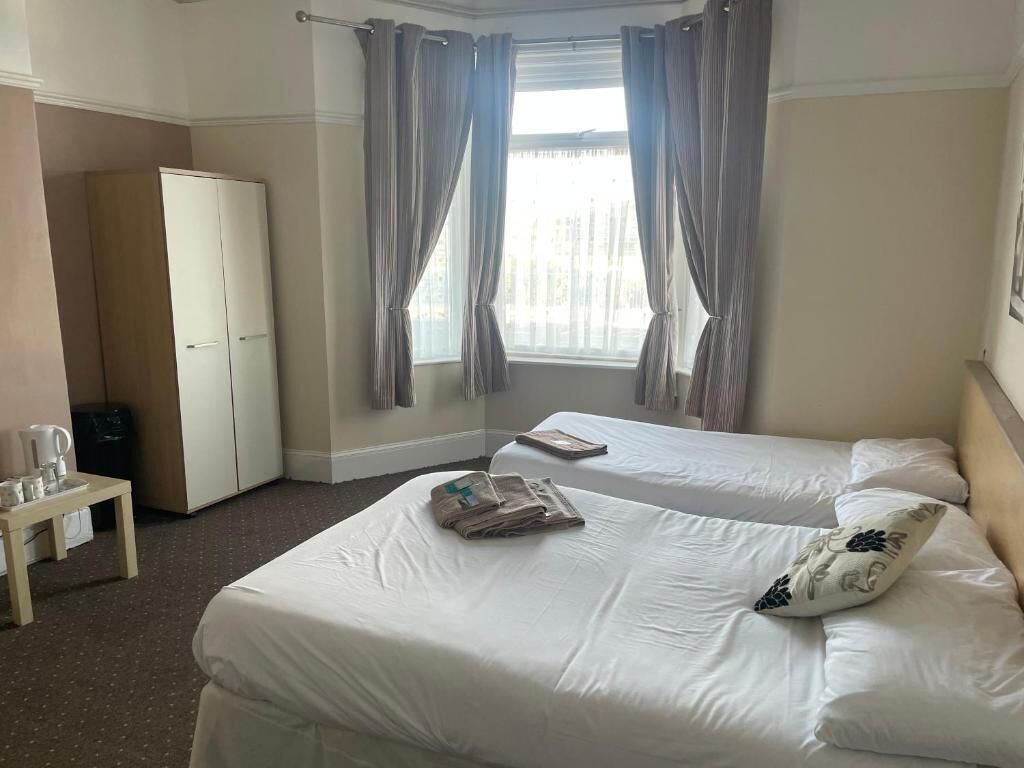Ett hotellrum med två sängar, en garderob, ett litet bord med en vattenkokare och ett fönster med gardiner.