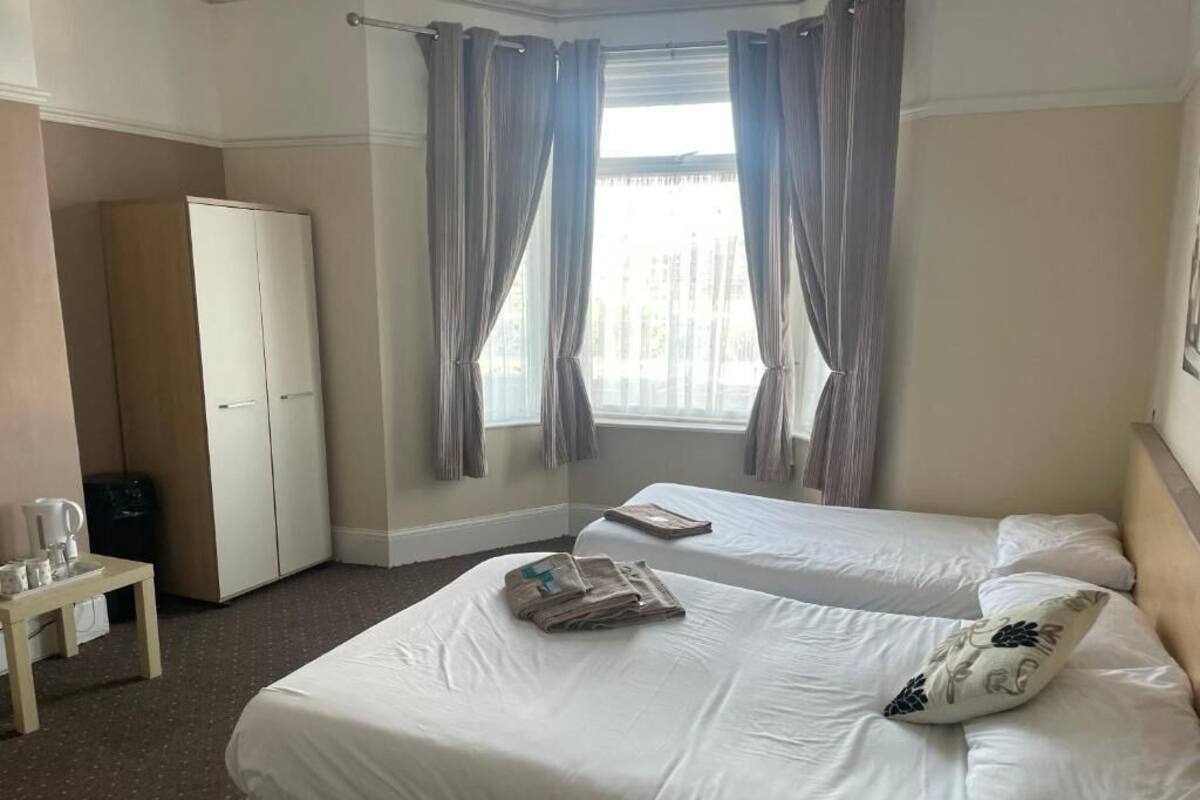 Ett hotellrum med två sängar, en garderob, ett litet bord med en vattenkokare och ett fönster med gardiner.