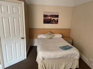 Ett hotellrum med en säng, ett nattduksbord, en dörr och en tavla som hänger på väggen.