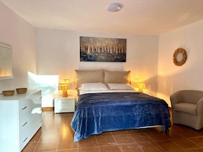 A bedroom with a bed, two bedside tables, a chair, a dresser, and a painting on the wall.