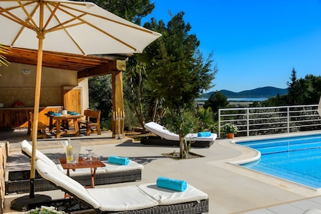 A poolside area with lounge chairs, a table, and a pergola with an umbrella.. Can Damià – Villa with Pool and Panoramic Sea Views in Sant Josep de sa Talaia, Ibiza