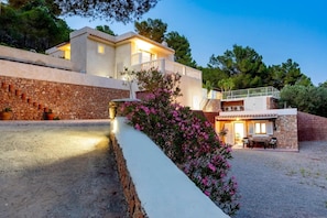 A two-story building with a stone wall, a balcony, and a small outdoor seating area.