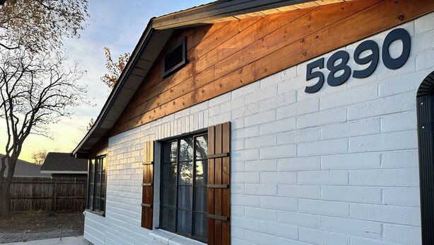 Ein weißes Ziegelgebäude mit der Nummer 5890, Holzfensterläden und einem sichtbaren Fenster.