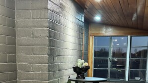 Eine Bar mit schwarzer Ziegelwand, Holzboden, einem grün-weißen Barhocker und einem kleinen Tisch mit einer Pflanze.