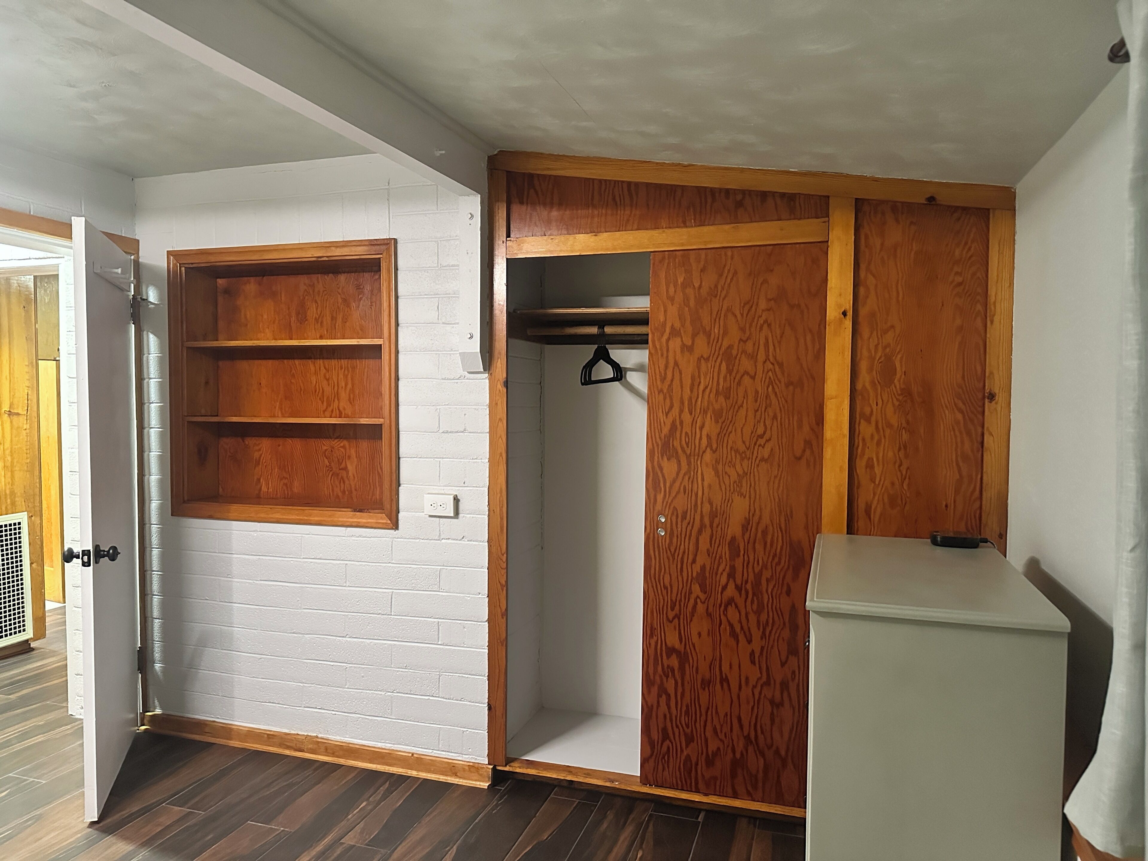 A room with a white brick wall, wooden wardrobe, and a white cabinet.