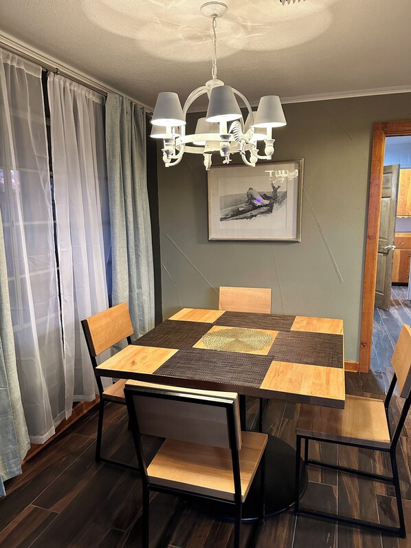 Un comedor con una mesa, sillas, una araña y un cuadro en la pared.