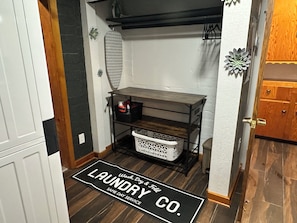 Un espace dédié à la lessive, avec un tapis noir, des étagères en bois et un panier.