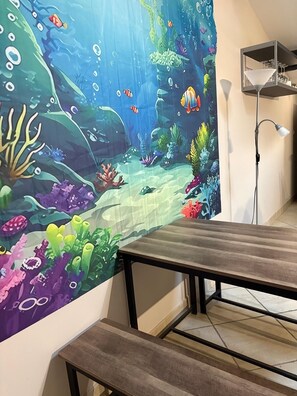 A room with a wooden bench, a wall-mounted shelf, and an underwater-themed tapestry. - Beautiful apartment with pool access (La Rouvière)