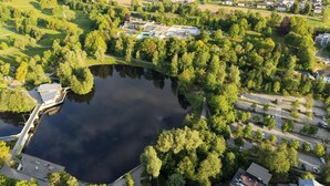 Vista aérea de una propiedad junto al lago con muelle, un edificio pequeño con paneles solares y vegetación circundante.