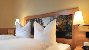 Habitación de hotel con dos camas, ropa de cama blanca, cabecero con pintura de temática natural y lámparas de noche.