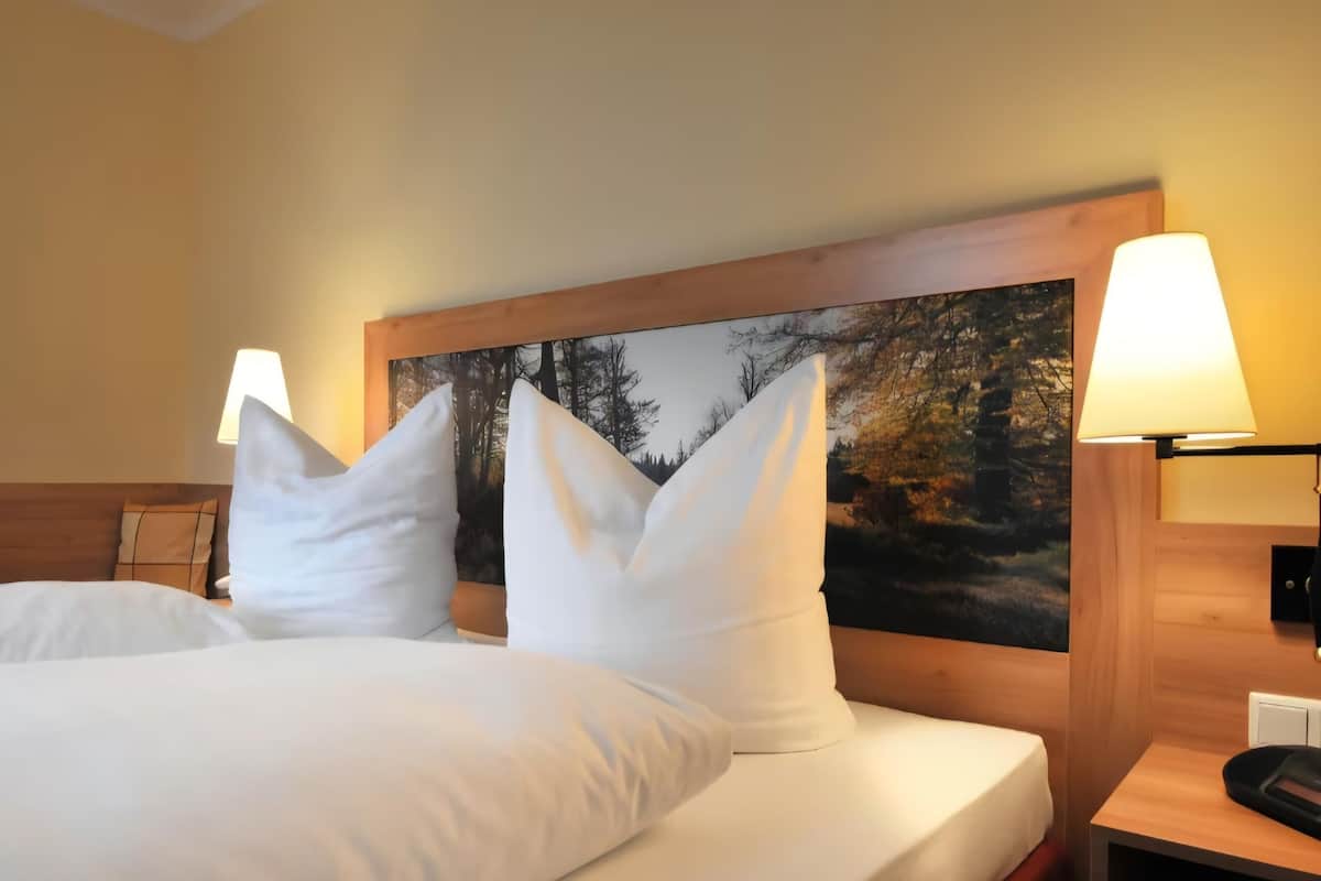 Habitación de hotel con dos camas, ropa de cama blanca, cabecero con pintura de temática natural y lámparas de noche.