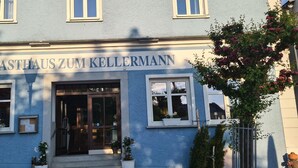 Un hotel llamado 'HOTEL GASTHAUS ZUM KELLERMANN' con una fachada tradicional, ventanas amplias y plantas en macetas.
