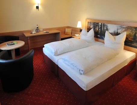 A hotel room with a bed, a desk, a chair, a small table, and a painting on the wall.. Hotel Zum Kellermann