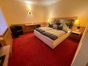 A hotel room with a bed, desk, chair, and two bedside lamps.