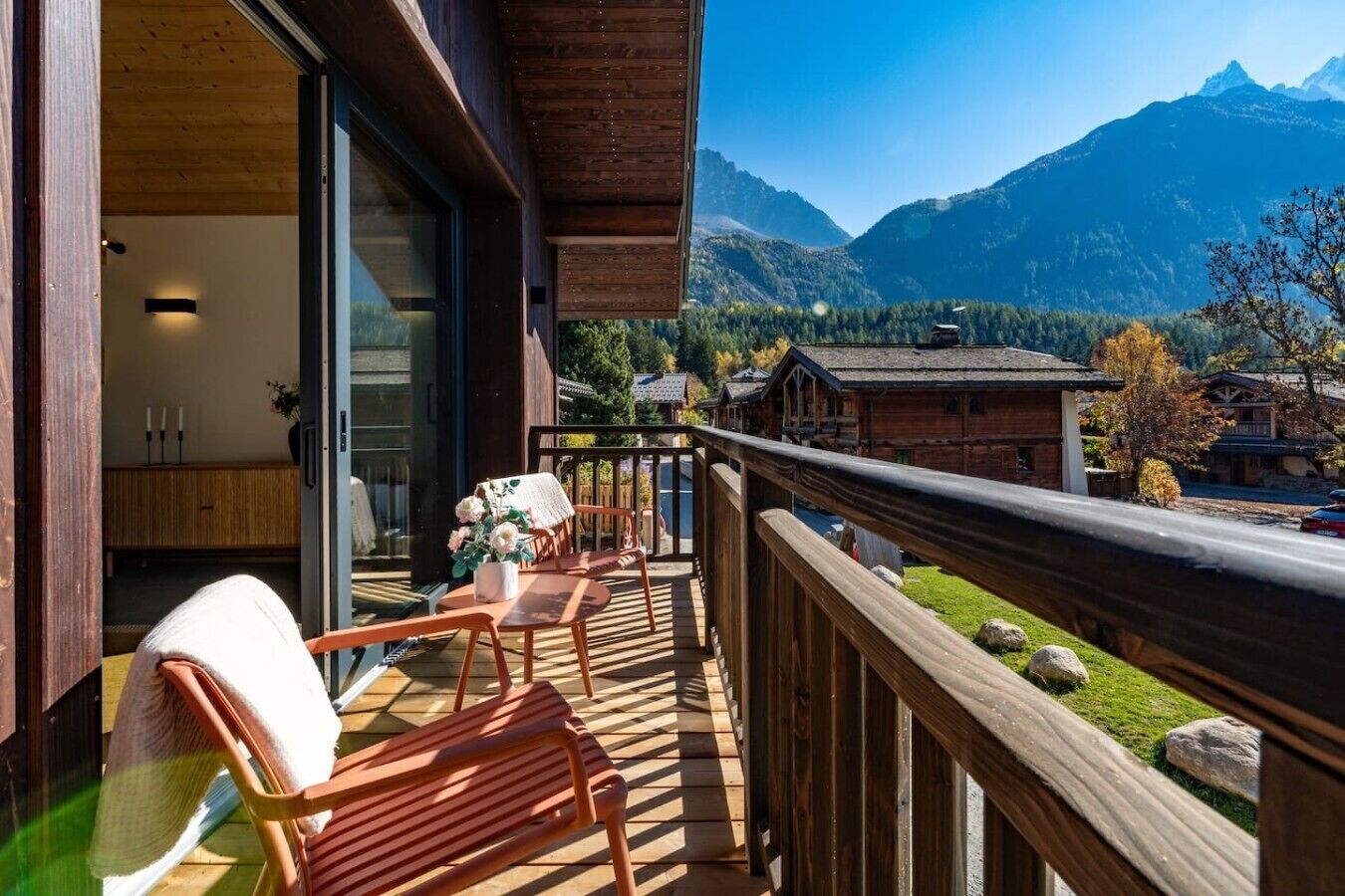 A balcony with wooden railings, a chair, a table, and a vase of flowers.