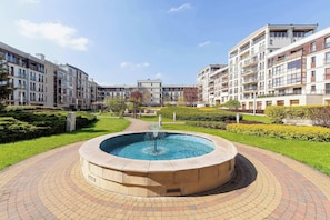 Um conjunto de edifícios residenciais com uma fonte circular central, caminhos pavimentados e áreas verdes bem cuidadas.