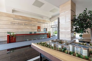 Uma receção com uma placa a indicar 'Garden Residence', uma maqueta de uma área residencial e uma grande planta de interior.