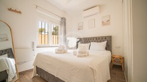 Un dormitorio con cama, espejo, ventana y aire acondicionado de pared.