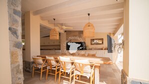 Un comedor con una mesa y sillas de madera, un ventilador de techo y una cocina al fondo.