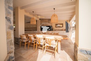Ein Essbereich mit Holztisch und -stühlen, einem Deckenventilator und einer Küche im Hintergrund.
