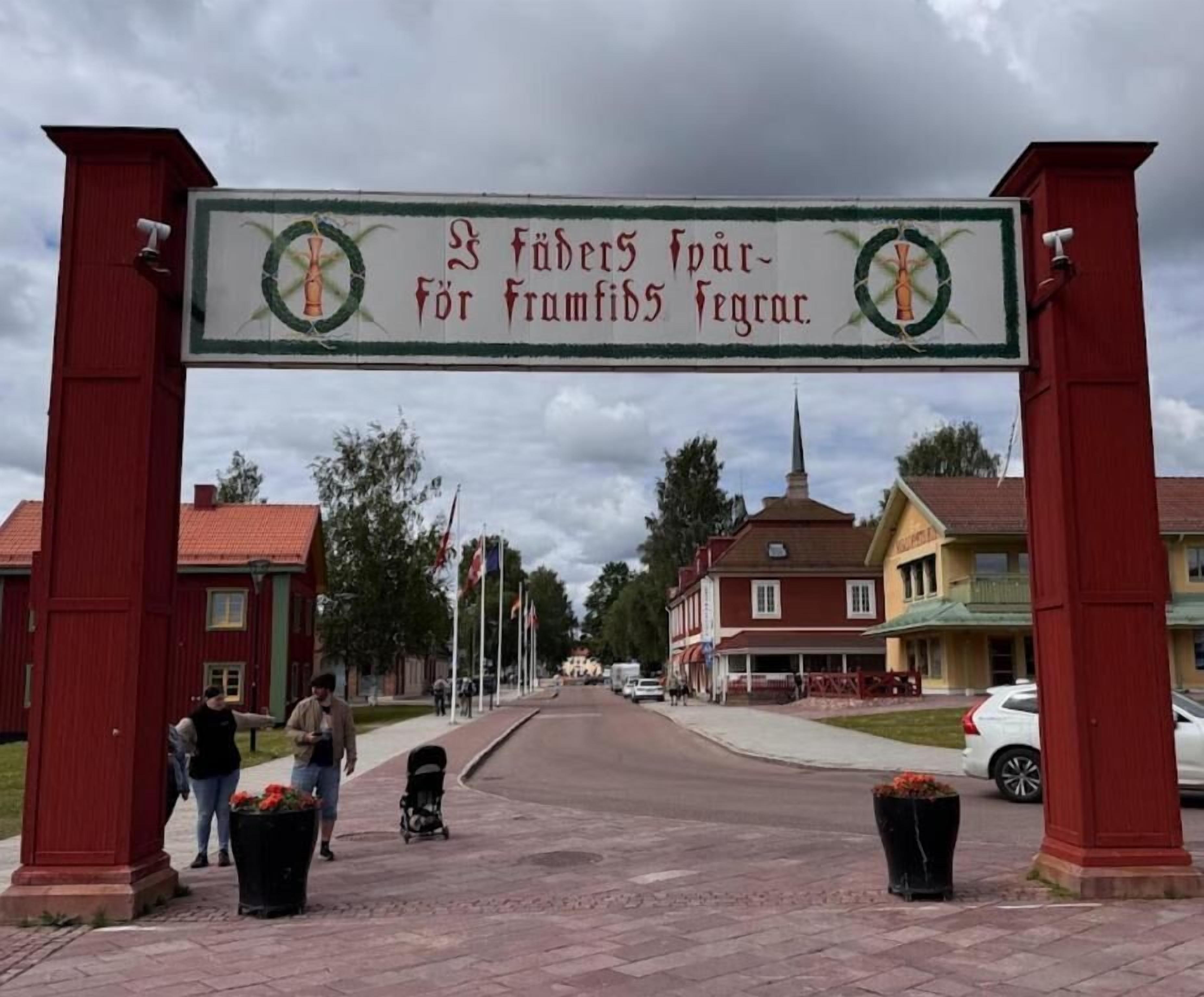 Une entrée donnant sur la rue, avec une enseigne, des bâtiments et, au fond, le clocher d’une église.
