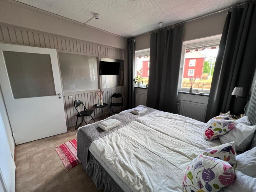 A bedroom with a bed, a desk, a chair, a window with curtains, and a view of a building outside.