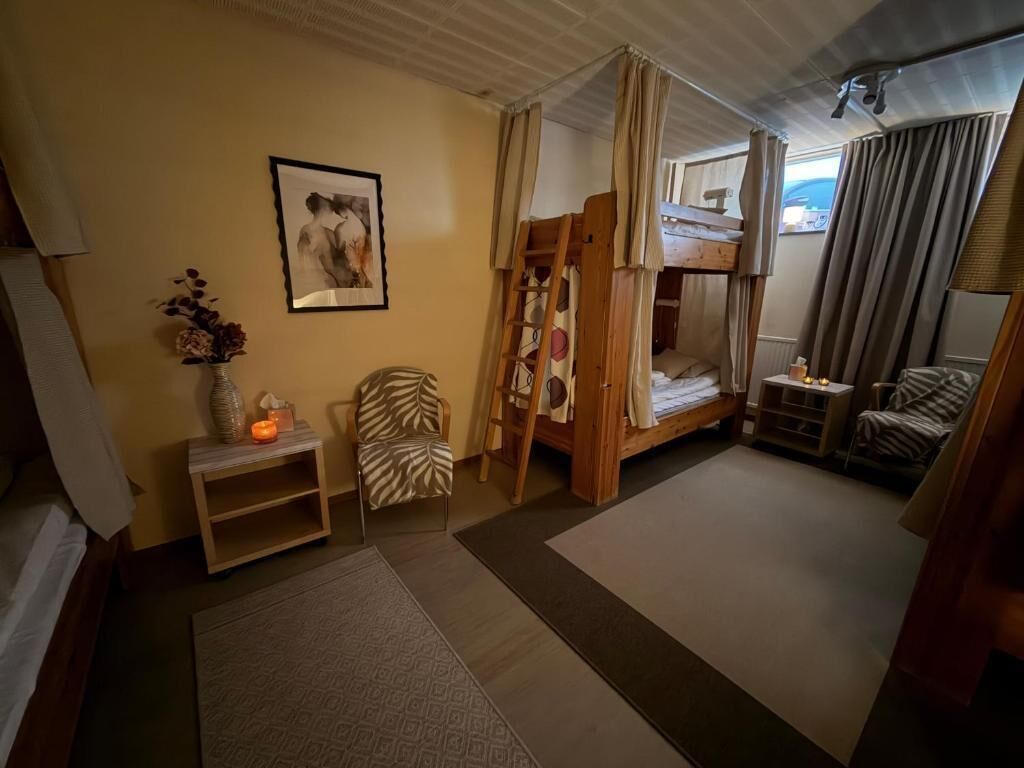 A room with bunk beds, a chair, a small table with a vase, and a framed picture on the wall.