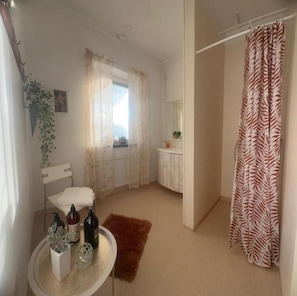 Un baño con cortina de ducha, inodoro, lavamanos y artículos de aseo, y una ventana con cortinas.