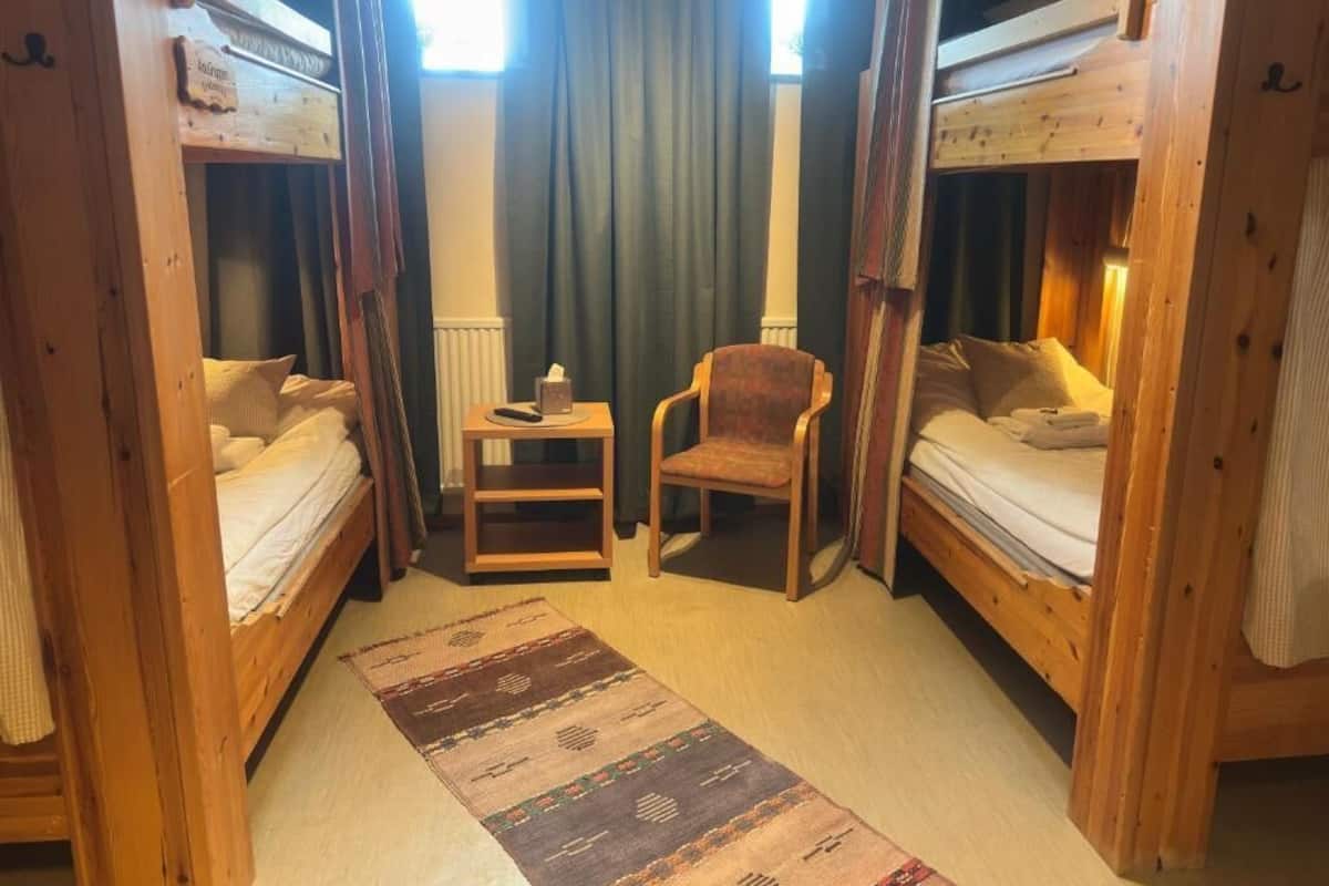 A room with two wooden bunk beds, a small wooden chair, a rug, and a window with curtains.