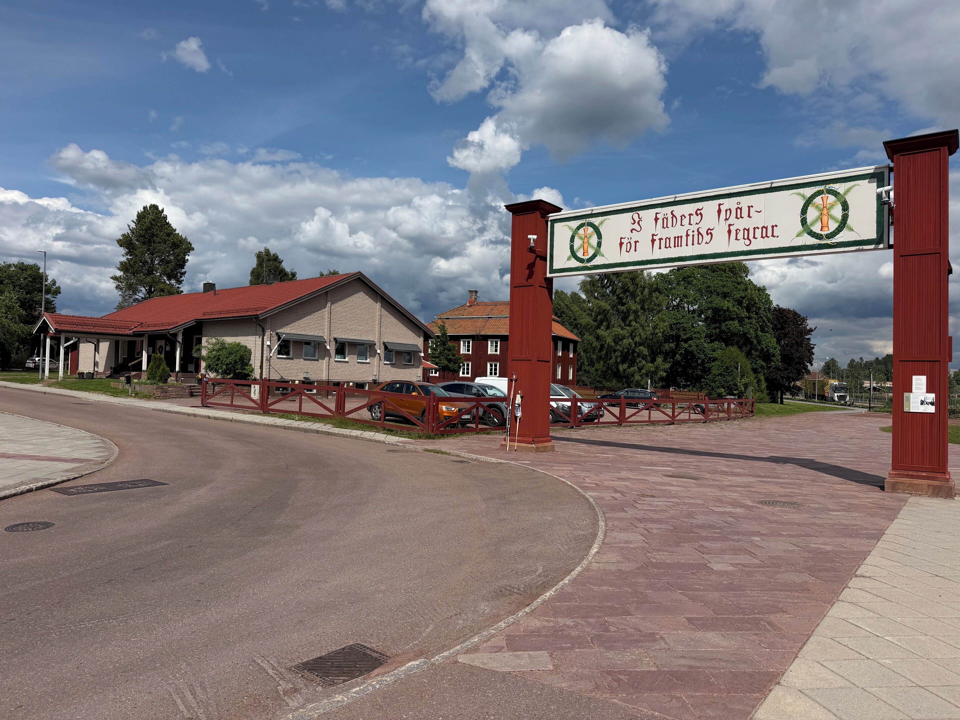 A building with a red roof, a sign with a green emblem, and a paved area with a fence.