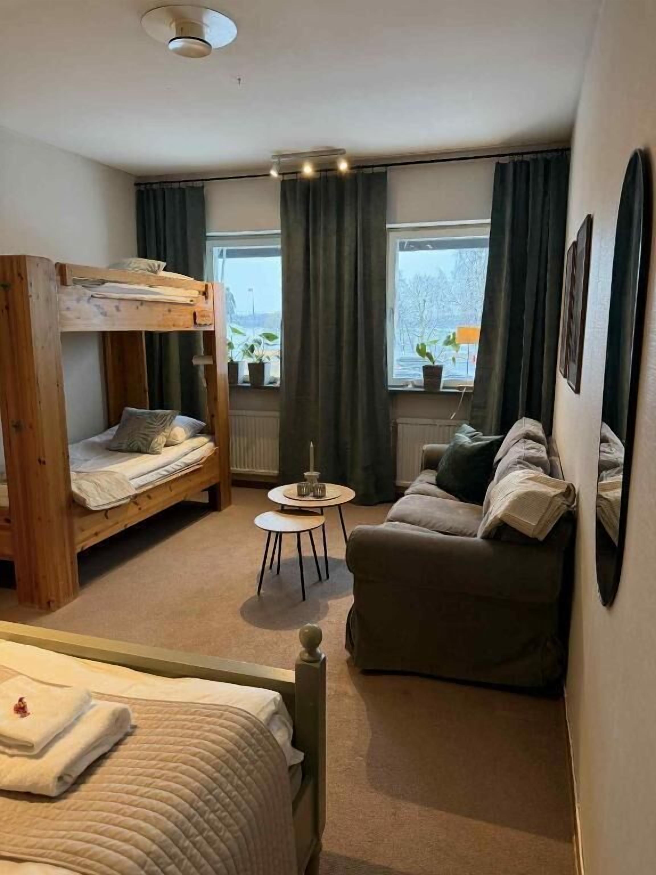 A room with a bunk bed, a sofa, a small round table, and a window with curtains.