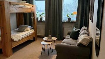 A room with a bunk bed, a sofa, a small round table, and a window with curtains.