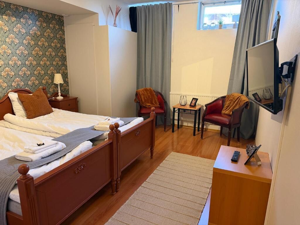 Quarto de hotel com cama de madeira, escrivaninha com cadeira, mesinha de centro com abajur e espelho na parede.