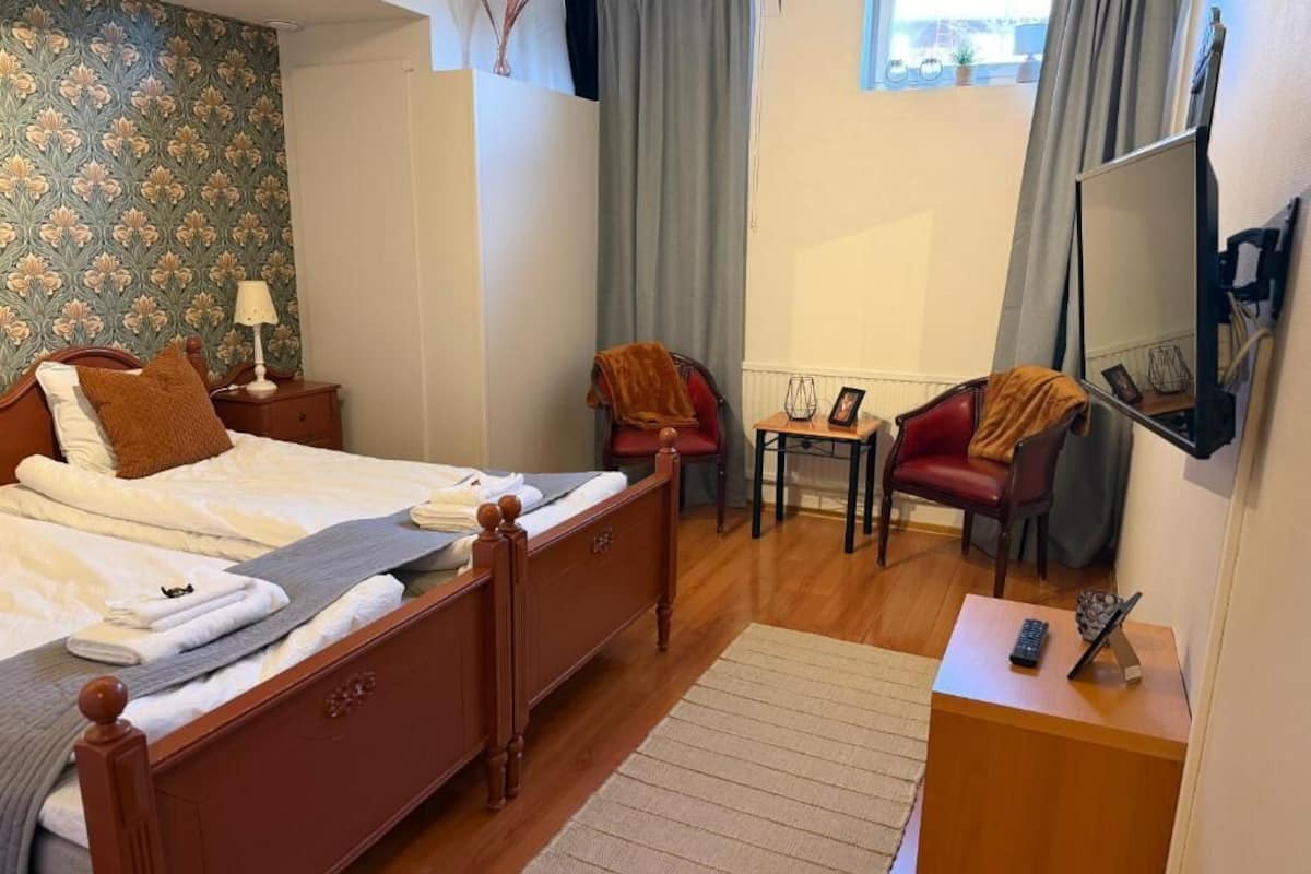 A hotel room with a wooden bed, a desk with a chair, a small table with a lamp, and a mirror on the wall.