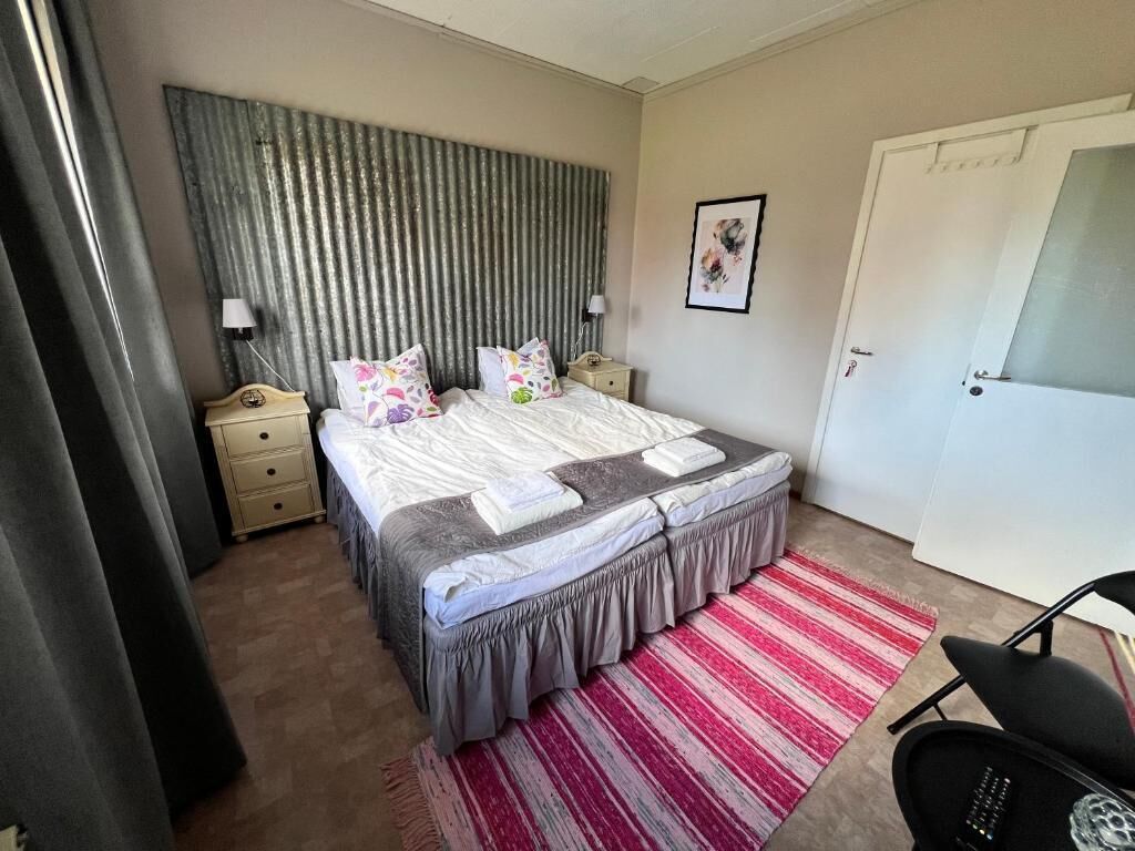 Ein Schlafzimmer mit Bett, Nachttischen, einem Sessel, einer Tür und einem Wandbild.