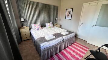 Ein Schlafzimmer mit Bett, Nachttischen, einem Sessel, einer Tür und einem Wandbild.