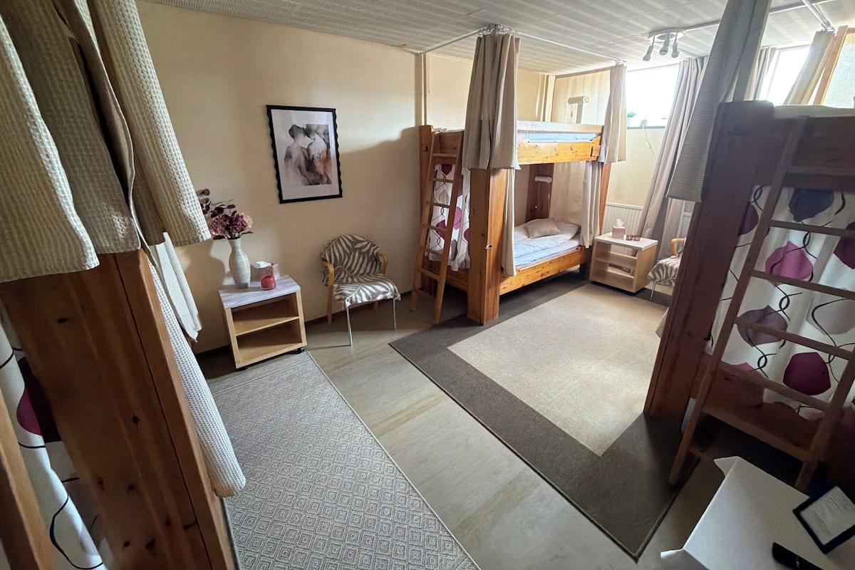 A room with a bunk bed, a chair, a small table, and a framed picture on the wall.