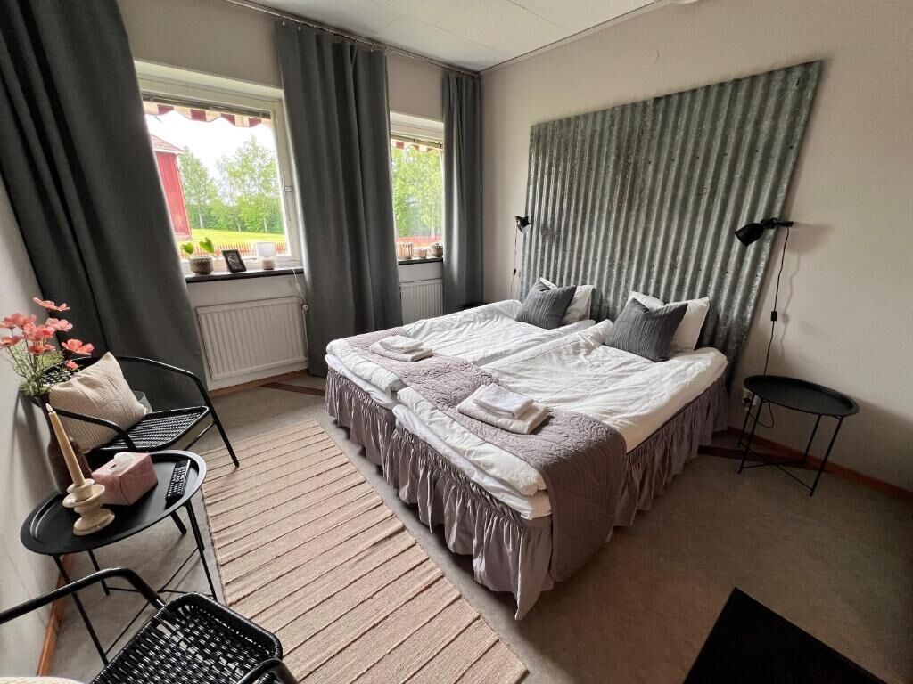 Un dormitorio con una cama grande, dos mesitas de noche, una silla, un radiador y una ventana con cortinas.