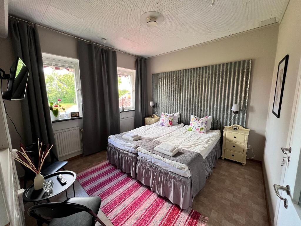 Quarto com cama, mesas de cabeceira, escrivaninha, cadeira, janela e cortinas.