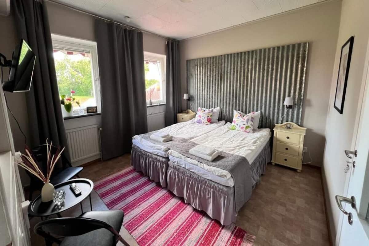 A bedroom with a bed, bedside tables, a desk, a chair, a window, and curtains.