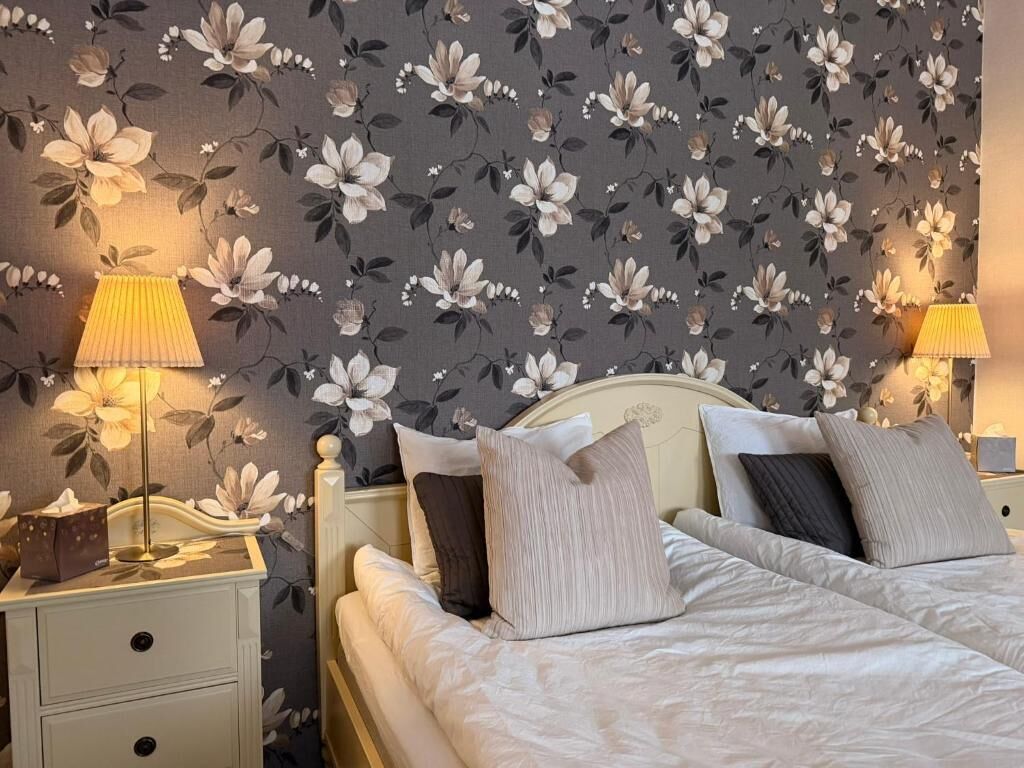 Uma cama bem arrumada com travesseiros, uma luminária de cabeceira e uma mesinha de cabeceira com caixa de lenços.