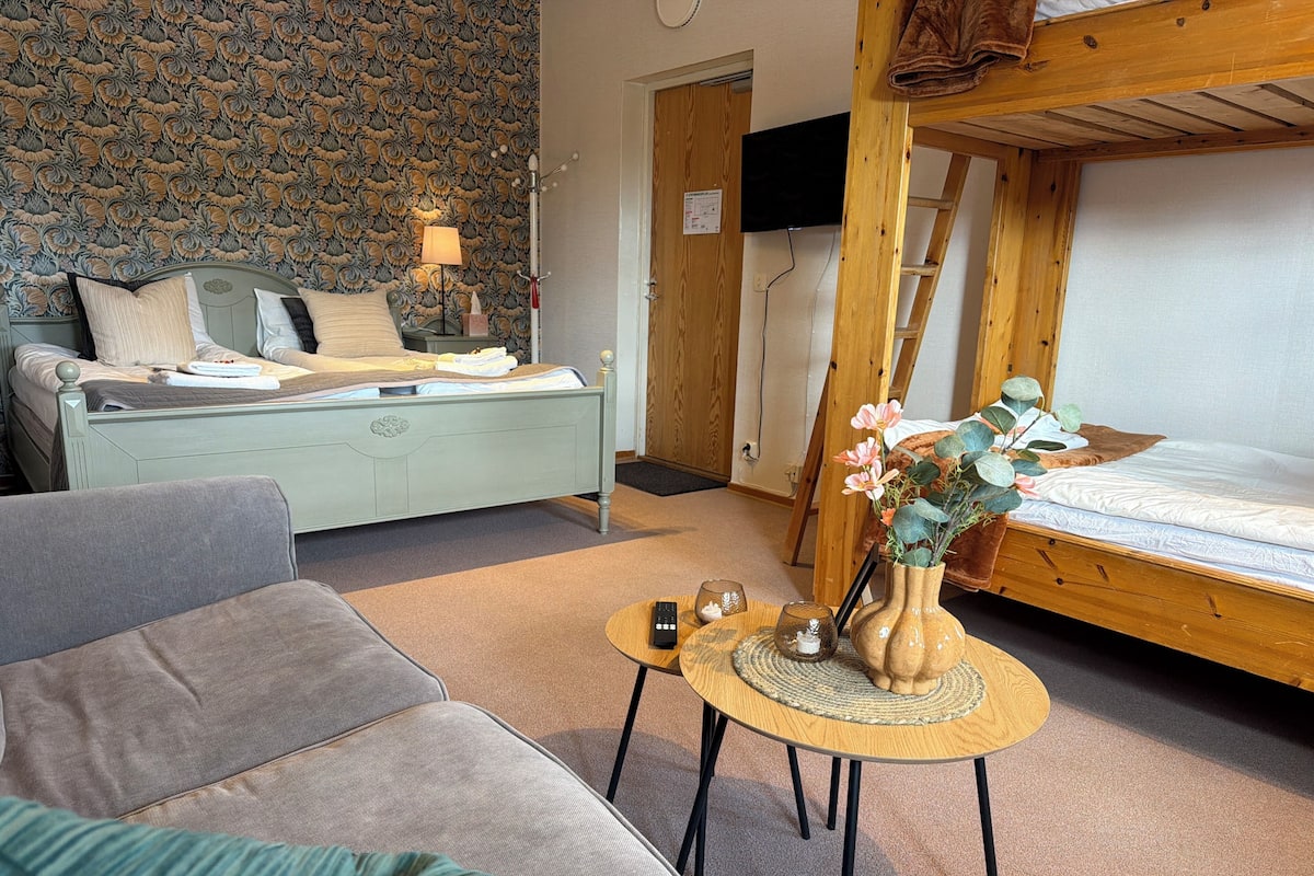A room with a bunk bed, a sofa, a small table with a vase, and a patterned wallpaper.
