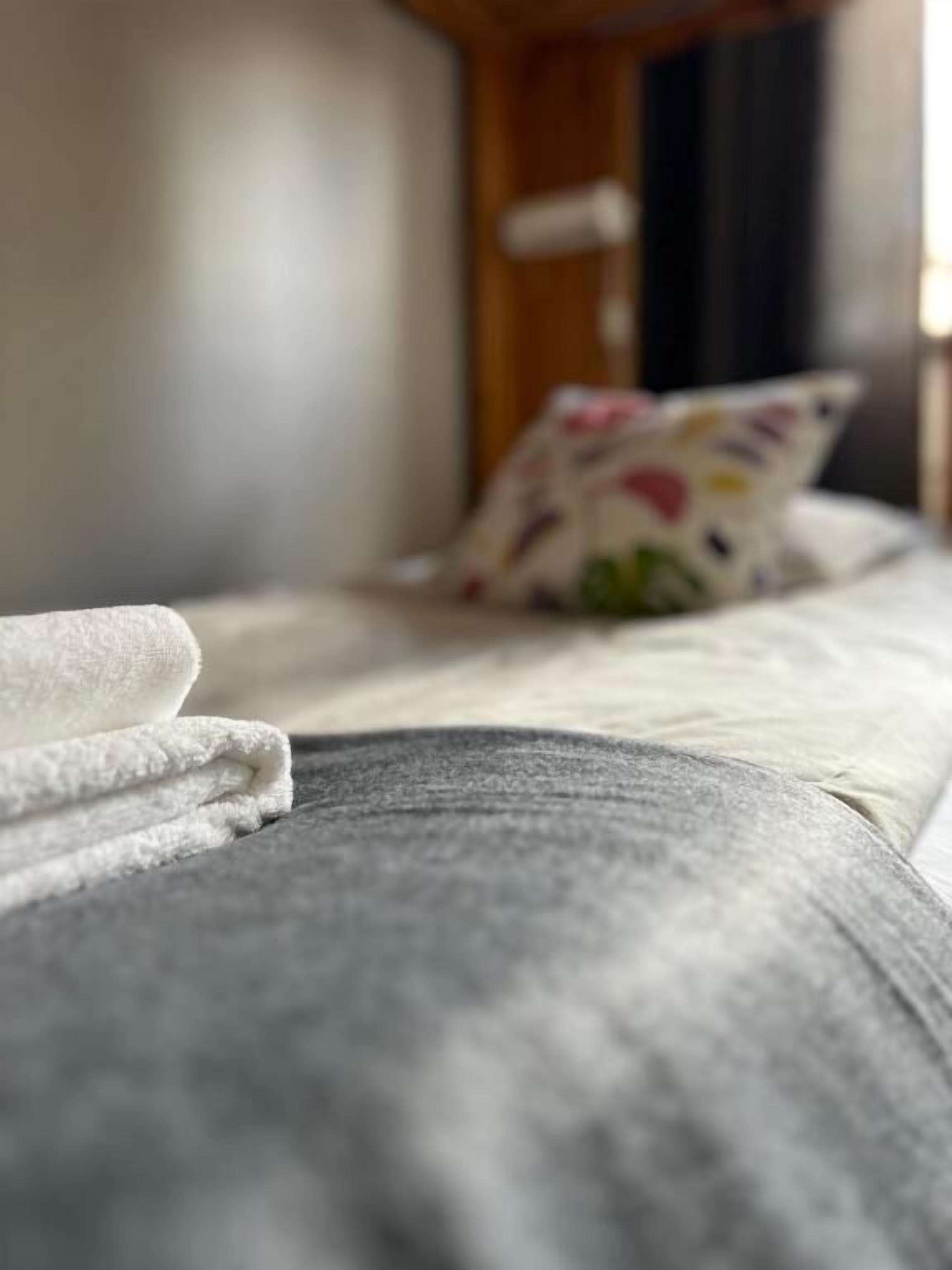 Una cama con una toalla blanca y un cojín estampado con motivos florales.