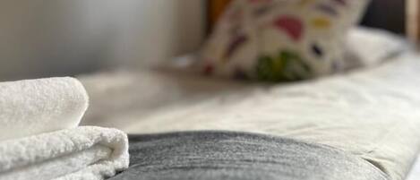 Una cama con una toalla blanca y un cojín estampado con motivos florales.