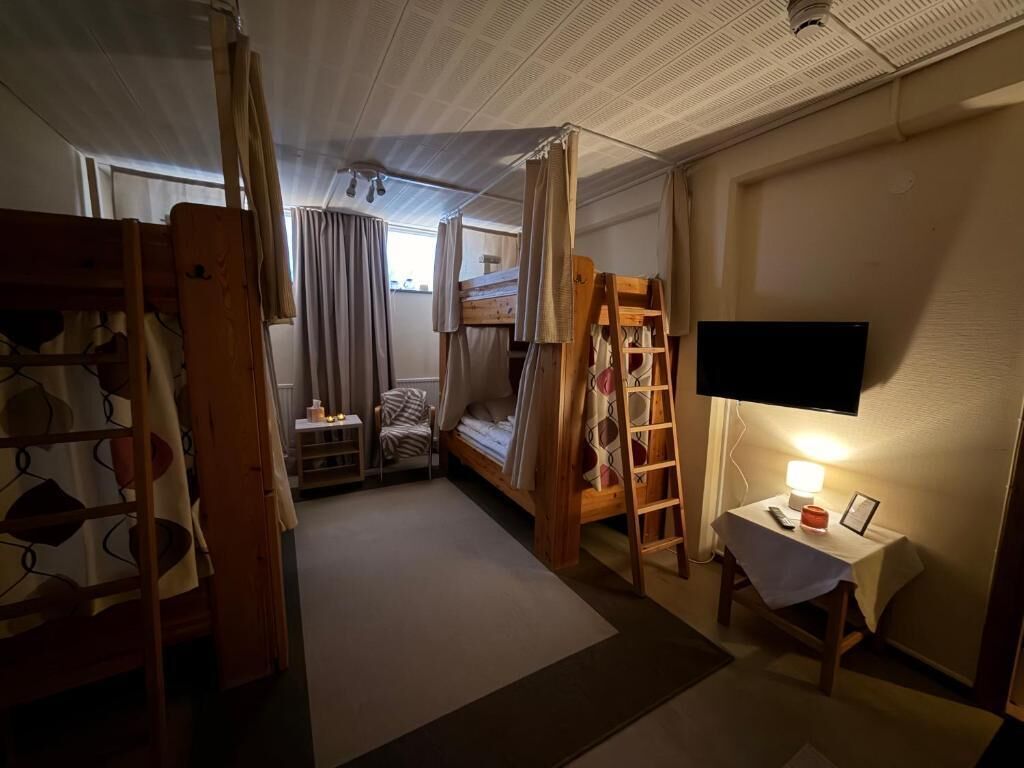 Quarto compacto com beliche, escada, pequena mesa com abajur e televisão na parede.