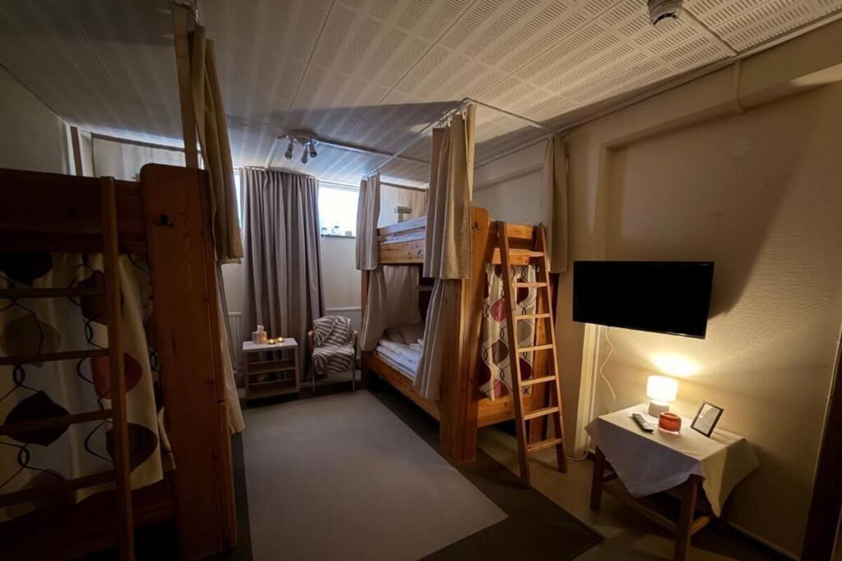 Quarto compacto com beliche, escada, pequena mesa com abajur e televisão na parede.