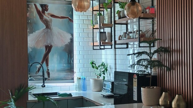 A modern kitchen with a central island, bar stools, pendant lighting, and a large poster of a ballet dancer.