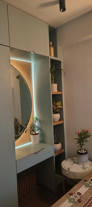 Um interior moderno com um espelho embutido, estantes com plantas, uma mesa redonda com tampo de mármore e toalha de mesa estampada.